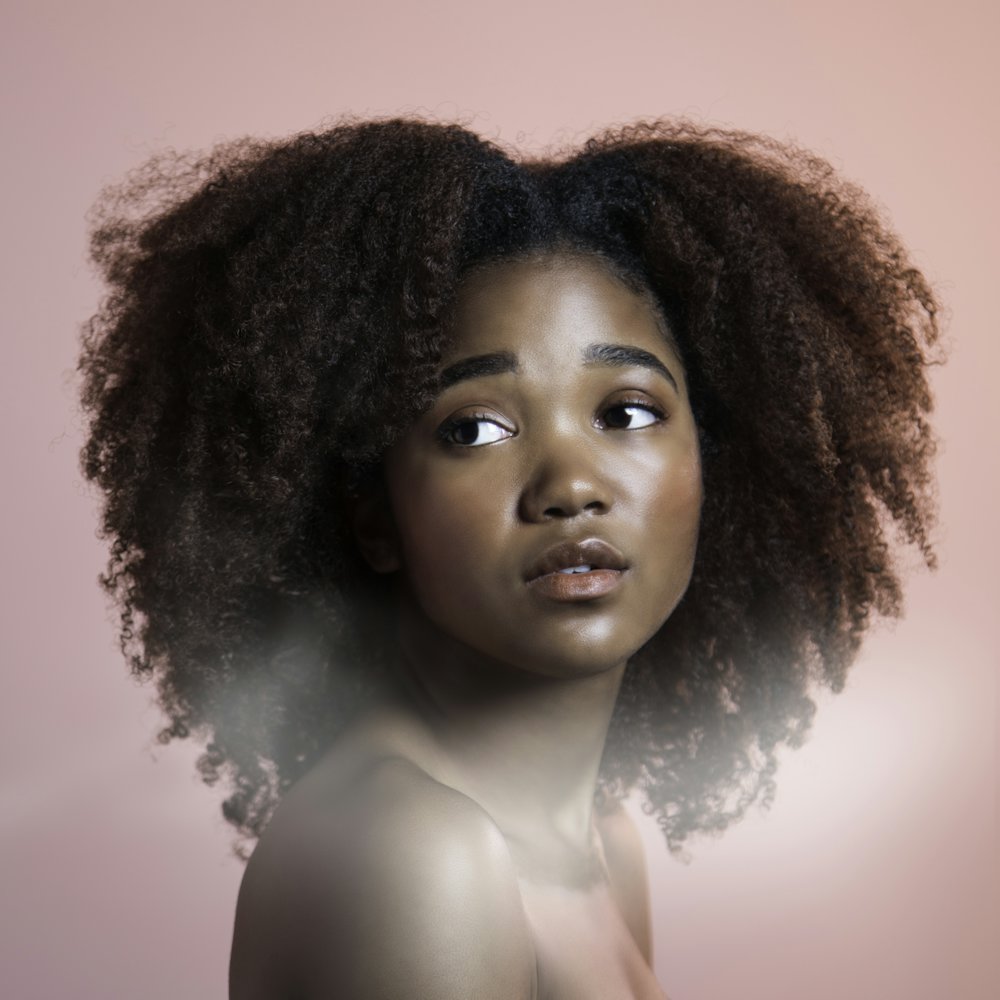 Jeune femme aux cheveux bouclés volumineux sur fond rose