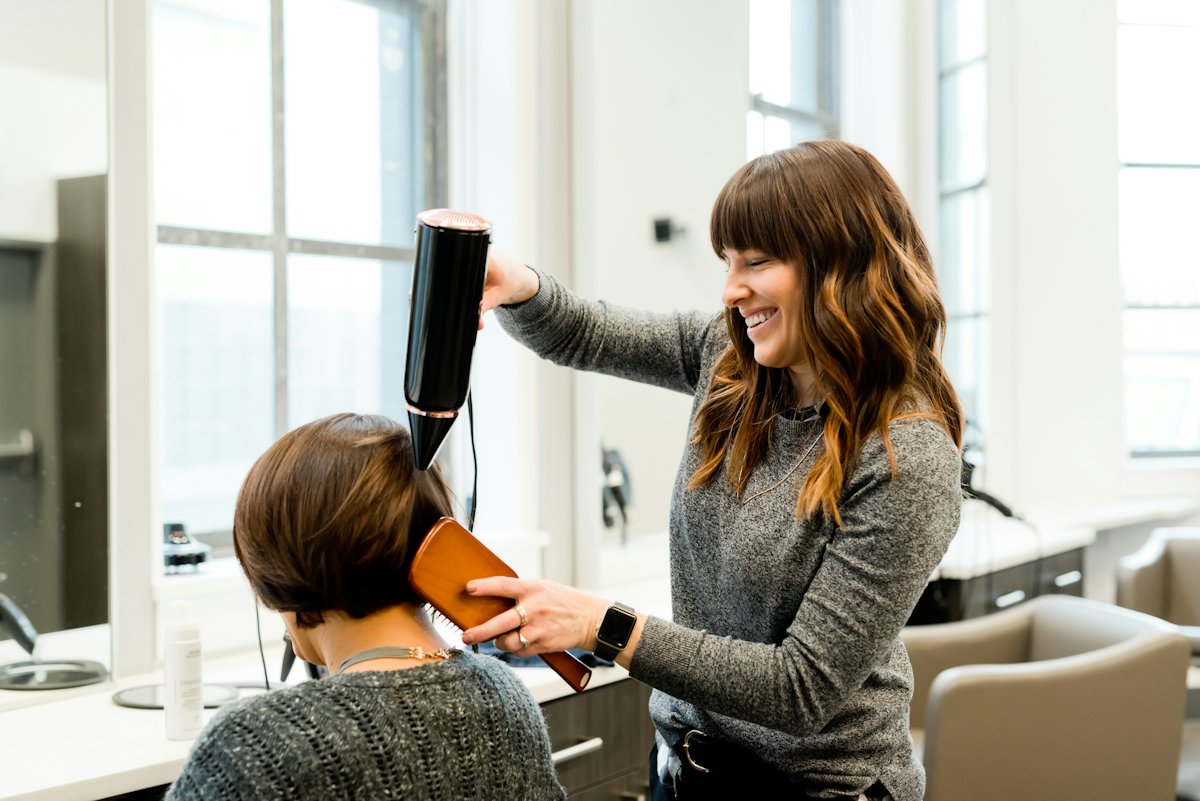 Coiffeuse souriante réalisant un brushing